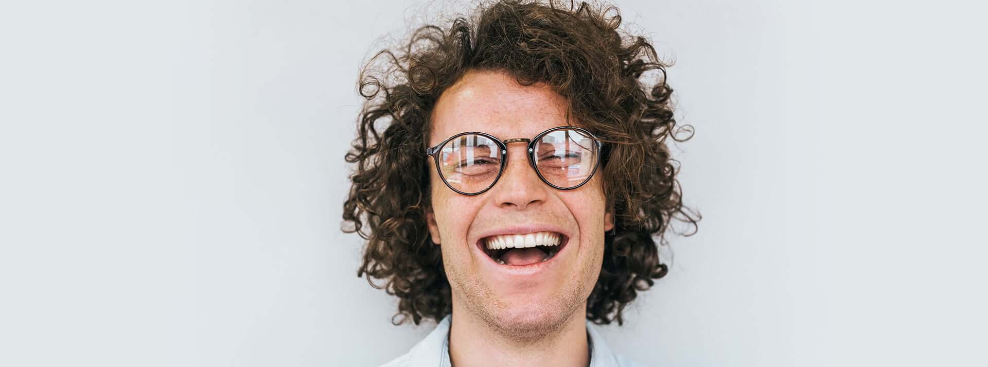 Man with curly hair and glasses laughing